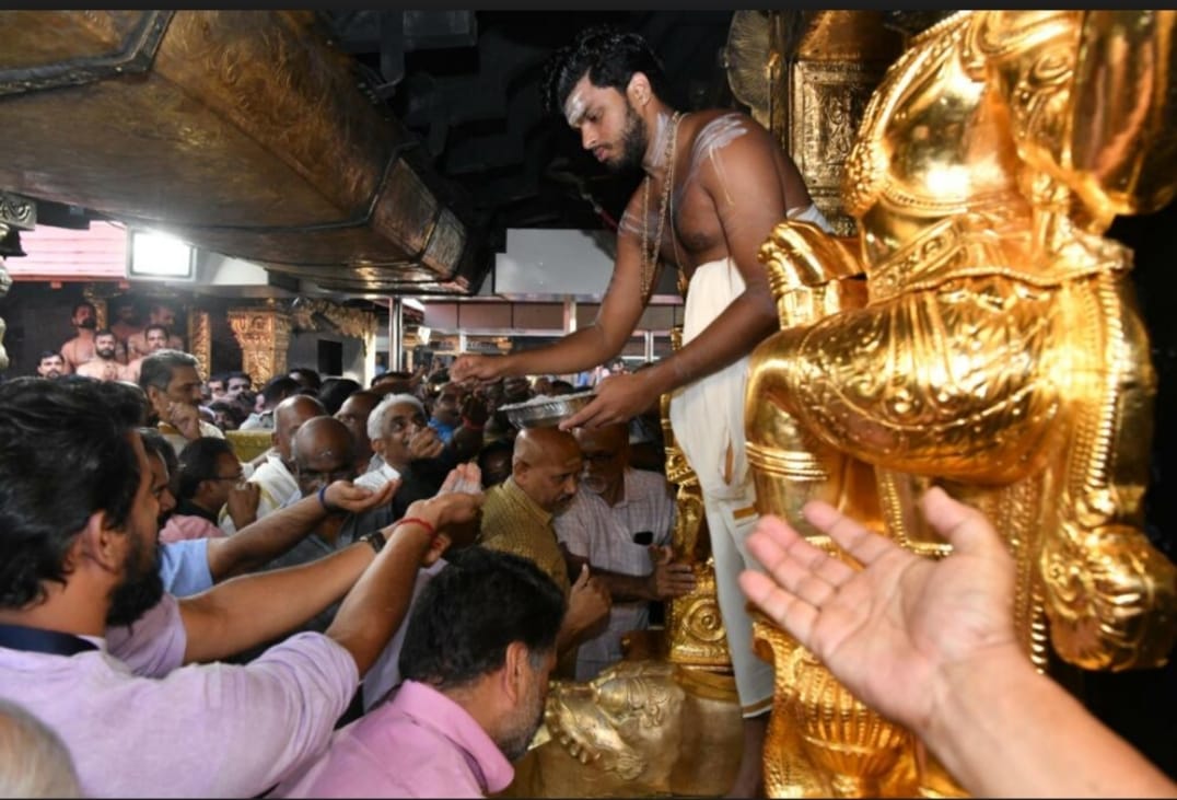 A priest distributing 'prasadam' by the gold-plated Dwarapalaka sculptures at Sabarimala.