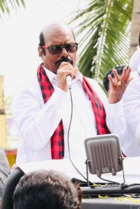 E. V. Velu speaking into a microphone at a public event. 