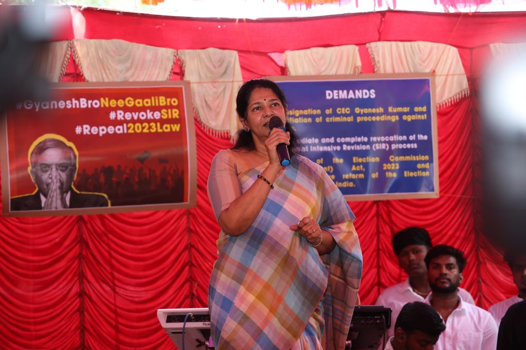 DMK Deputy General Secretary and MP Kanimozhi Karunanidhi addresses a gathering at a Chennai protest against SIR, speaking into a microphone in front of banners demanding Chief Election Commissioner Gyanesh Kumar’s resignation and the repeal of the 2023 law governing the appointment of election commissioners.