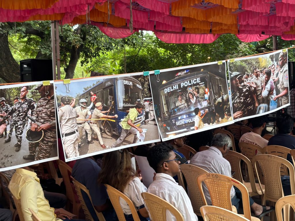 Photographs showing police personnel confronting and detaining protesters are displayed on a line beneath a colourful canopy at a public gathering.